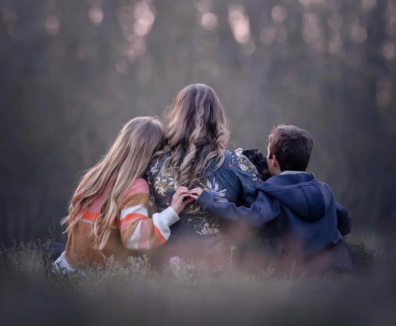 12 family photography poses for natural smiles in san diego 2 Heartwarming family photography poses moment with a mother and two children embracing in a soft, dreamy outdoor setting. Fine art family photography by Kat De Laet, capturing emotional connections in San Diego.