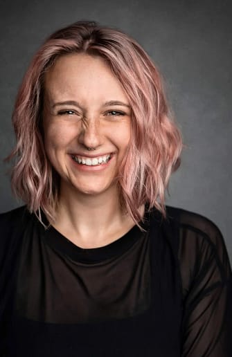 Woman with pink hair, smiling on a grey backdrop