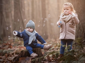 Kids-blowing-bubbles-forest-winter family photo session Young child playing with soap bubbles in a soft autumn setting, full of wonder. Magical children's photography by Kat De Laet, San Diego.