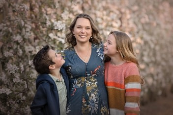 Mother-with-kids-in-flower-field family photo session Two children leaning on an adult in front of blooming trees.