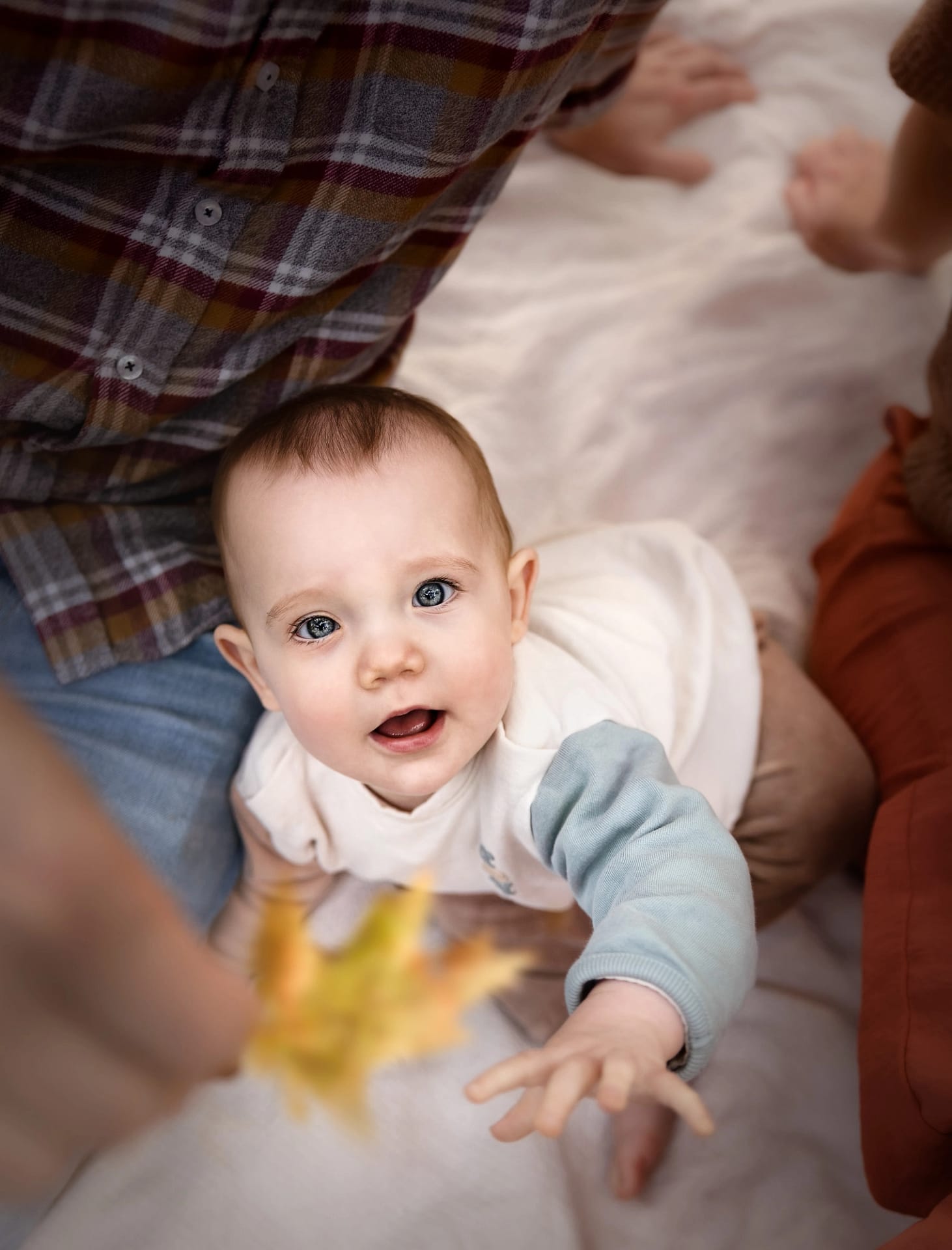 Baby with bright blue eyes reaching towards the camera – heartfelt family photography