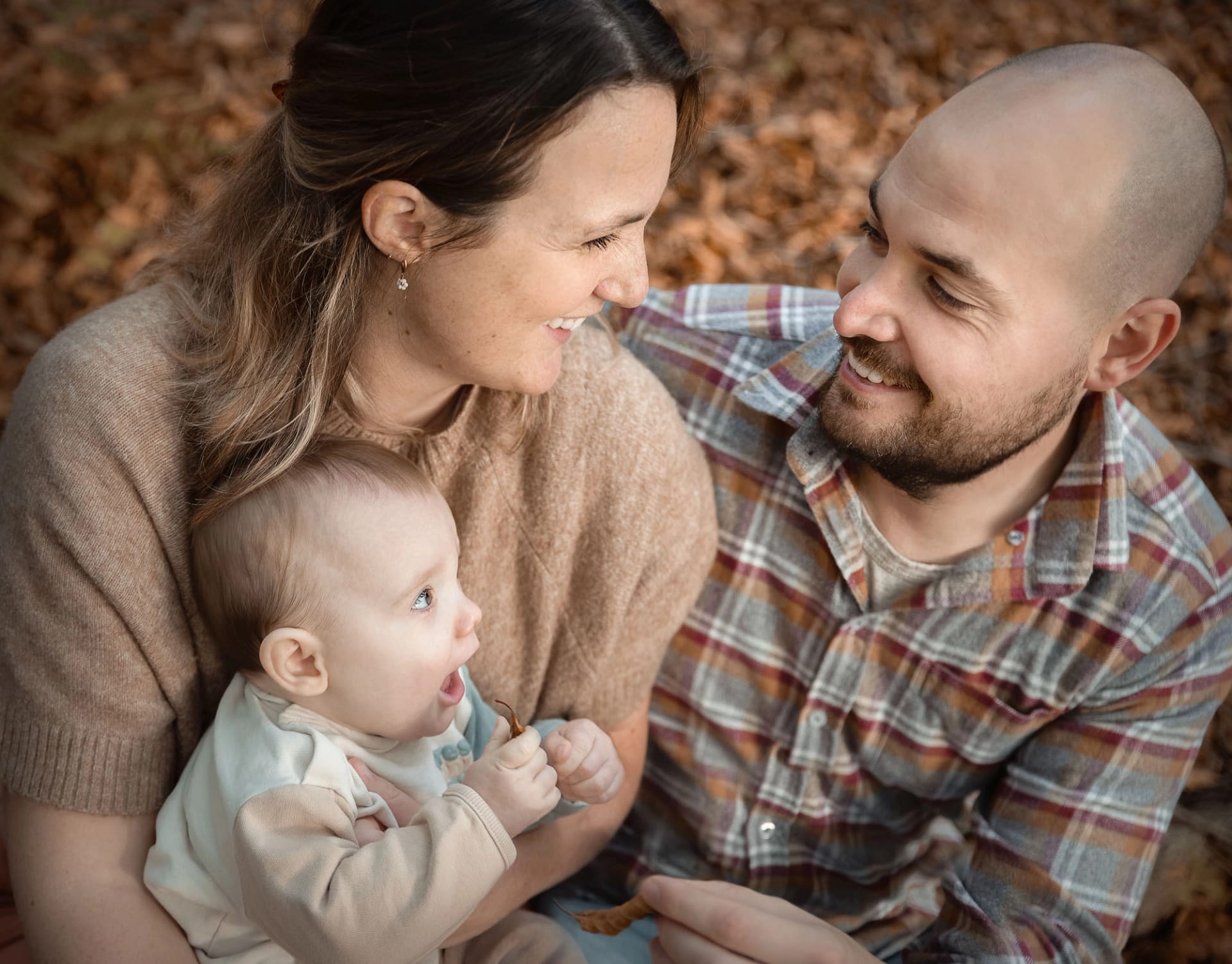 Heartwarming family moment featuring parents with their baby, wrapped in a cozy autumn setting.