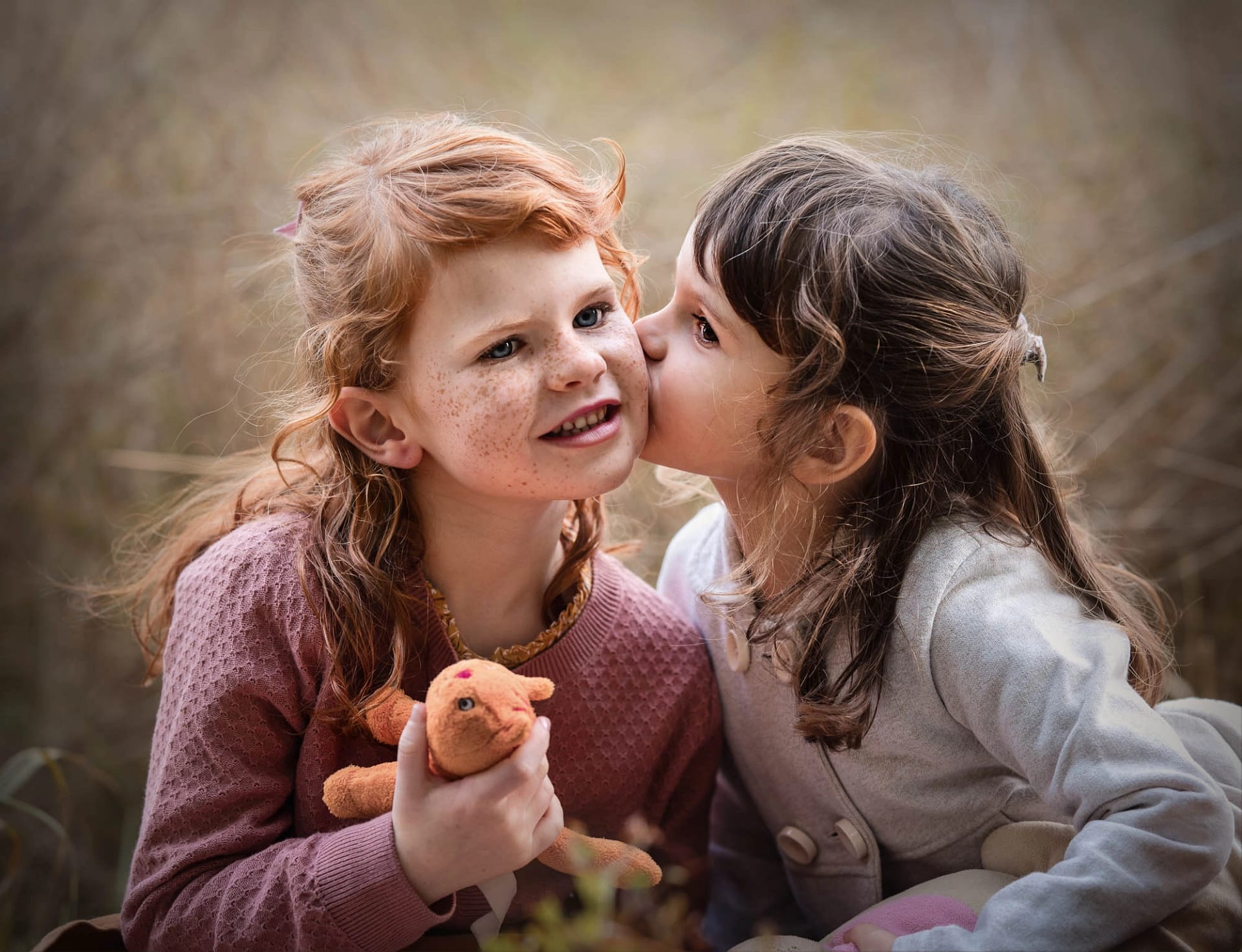 Two young girls sharing a sweet moment, one whispering into the other's ear. Heartfelt childhood portrait photography by Kat De Laet, San Diego.