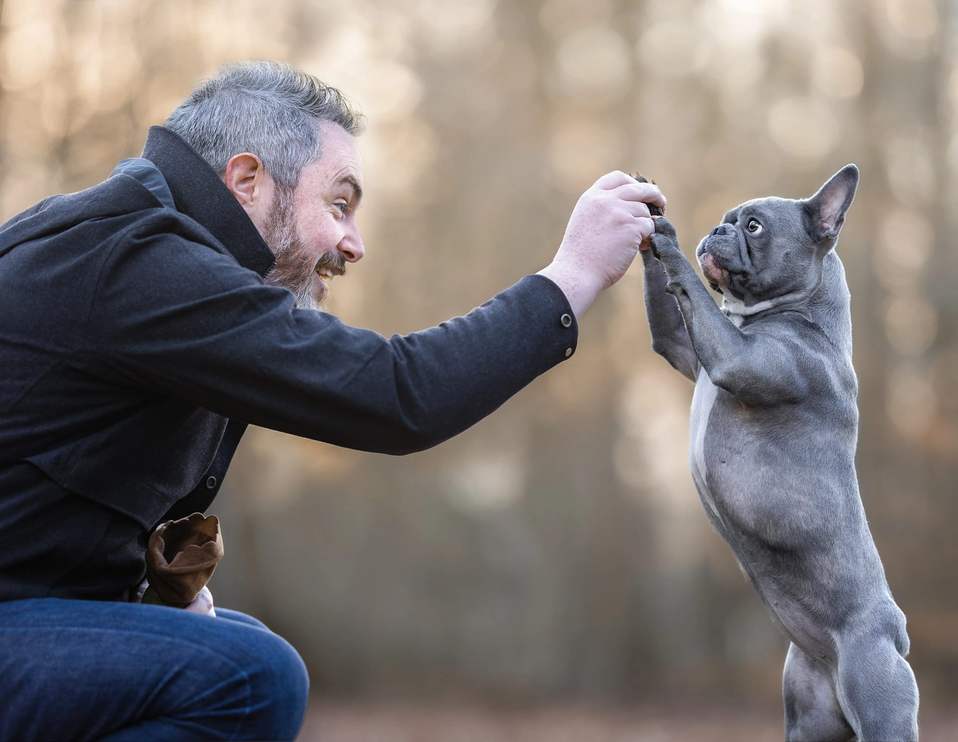 Man and his French Bulldog high-fiving in a wooded setting. Fun and engaging pet photography by Kat De Laet, San Diego.