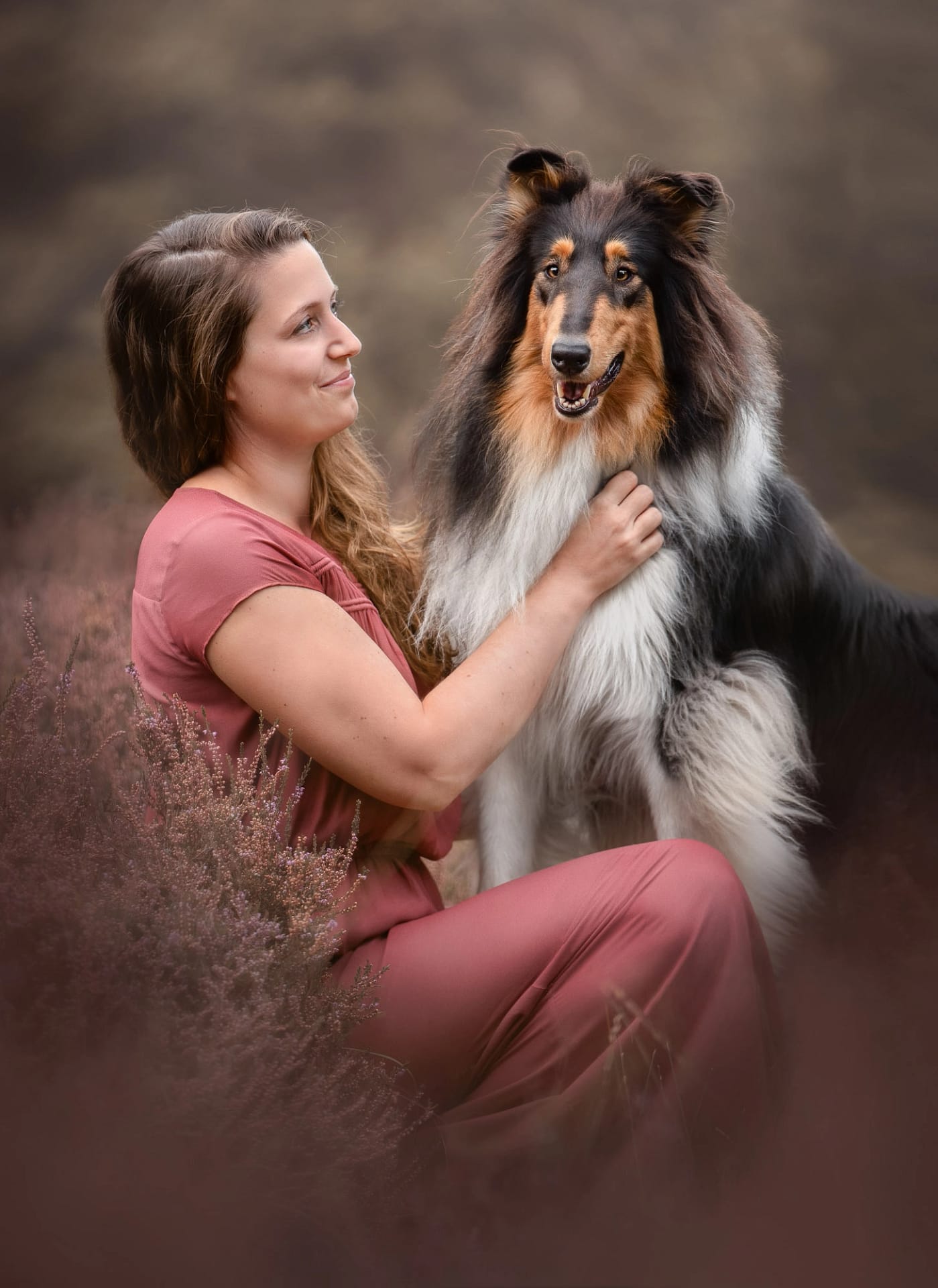 Woman in a pink dress posing with a majestic Collie, surrounded by a soft, muted outdoor landscape. Fine art dog photography by Kat De Laet, San Diego.